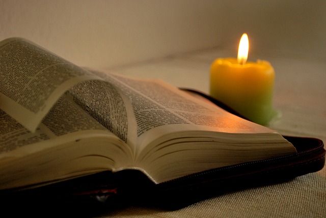 Avattu Raamattu ja palava keltainen kynttilä.