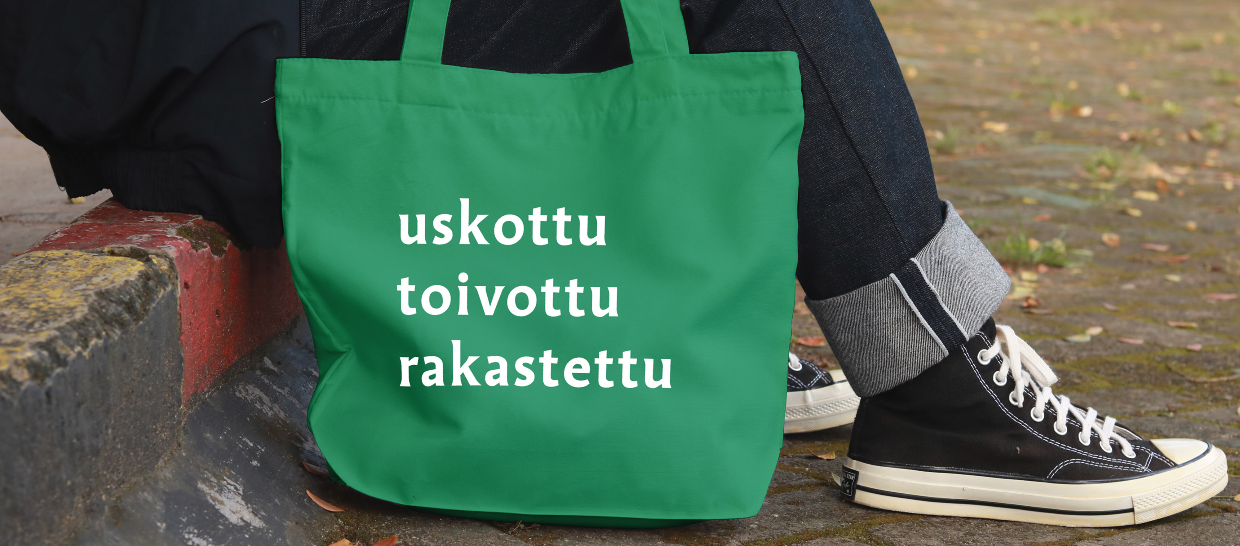 Kangaskassi, jossa teksti ”uskottu, toivottu, rakastettu”, henkilön vierellä ulkona.